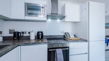 A modern kitchen with white cabinetry, a stainless steel range hood, a built-in microwave, and a refrigerator.