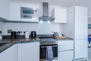 A modern kitchen with white cabinetry, a stainless steel range hood, a built-in microwave, and a refrigerator. - Modern 2 Bed Duplex Free Parking Wi Fi (Salford)