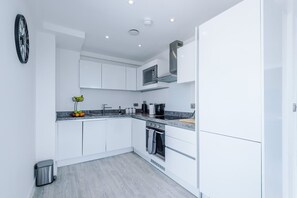 A modern kitchen with white cabinets, a microwave, a stove, and a fruit basket. - Modern 2 Bed Duplex Free Parking Wi Fi (Salford)