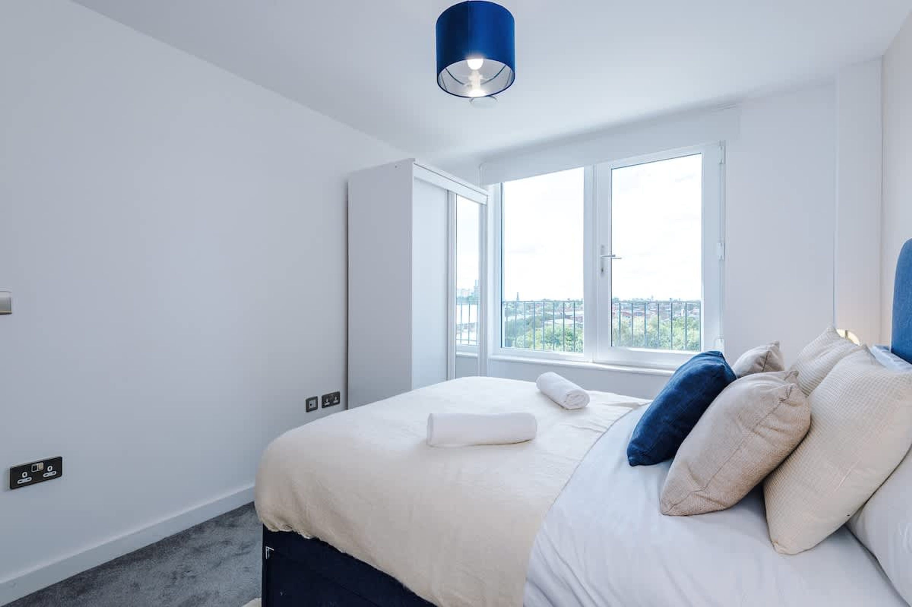 A modern bedroom with a large bed, a window with a view, and a blue pendant light.