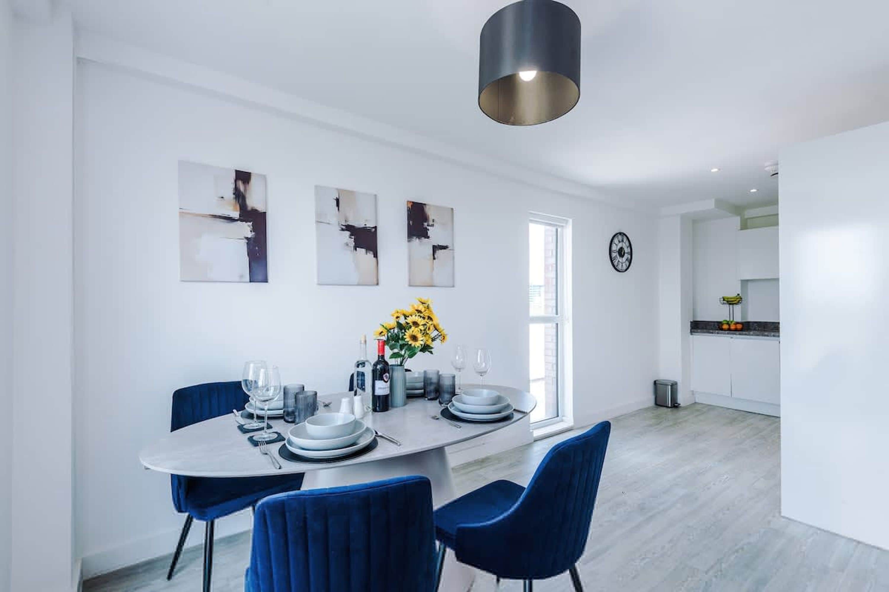 A modern dining area with a round table, blue chairs, and abstract wall art.
