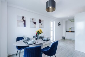 Een moderne eetruimte met een ronde tafel, blauwe stoelen en abstracte muurkunst.