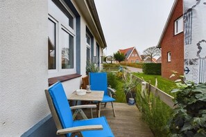 Een balkon met een tafel en stoelen, een uitzicht op een tuin, en een gebouw met een bakstenen gevel.