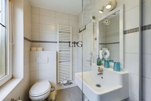 Een badkamer met toilet, een witte radiator, een douche met glazen wanden en een wastafel met blauwe glazen flessen.