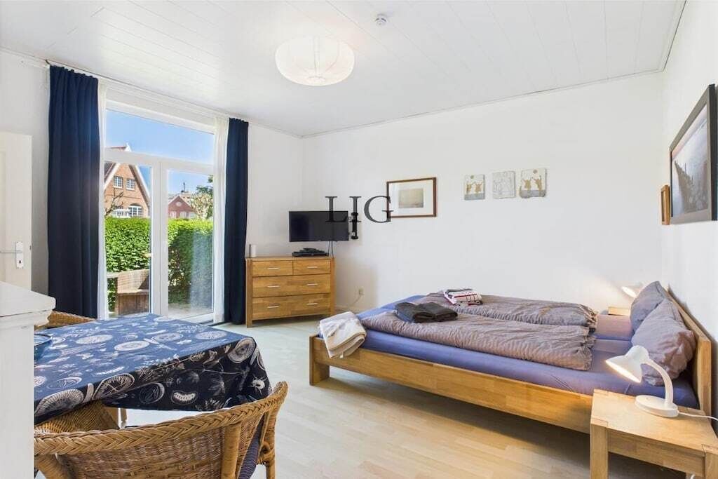 A bedroom with a bed, a TV, a dresser, and a window with curtains.