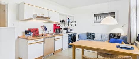 Ett kompakt bostadsutrymme med ett litet kök, en matplats och en sittgrupp med en soffa och kuddar.