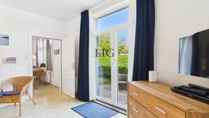 Una sala de estar moderna con televisor, un mueble de madera y un amplio ventanal corredizo que da a un espacio exterior.