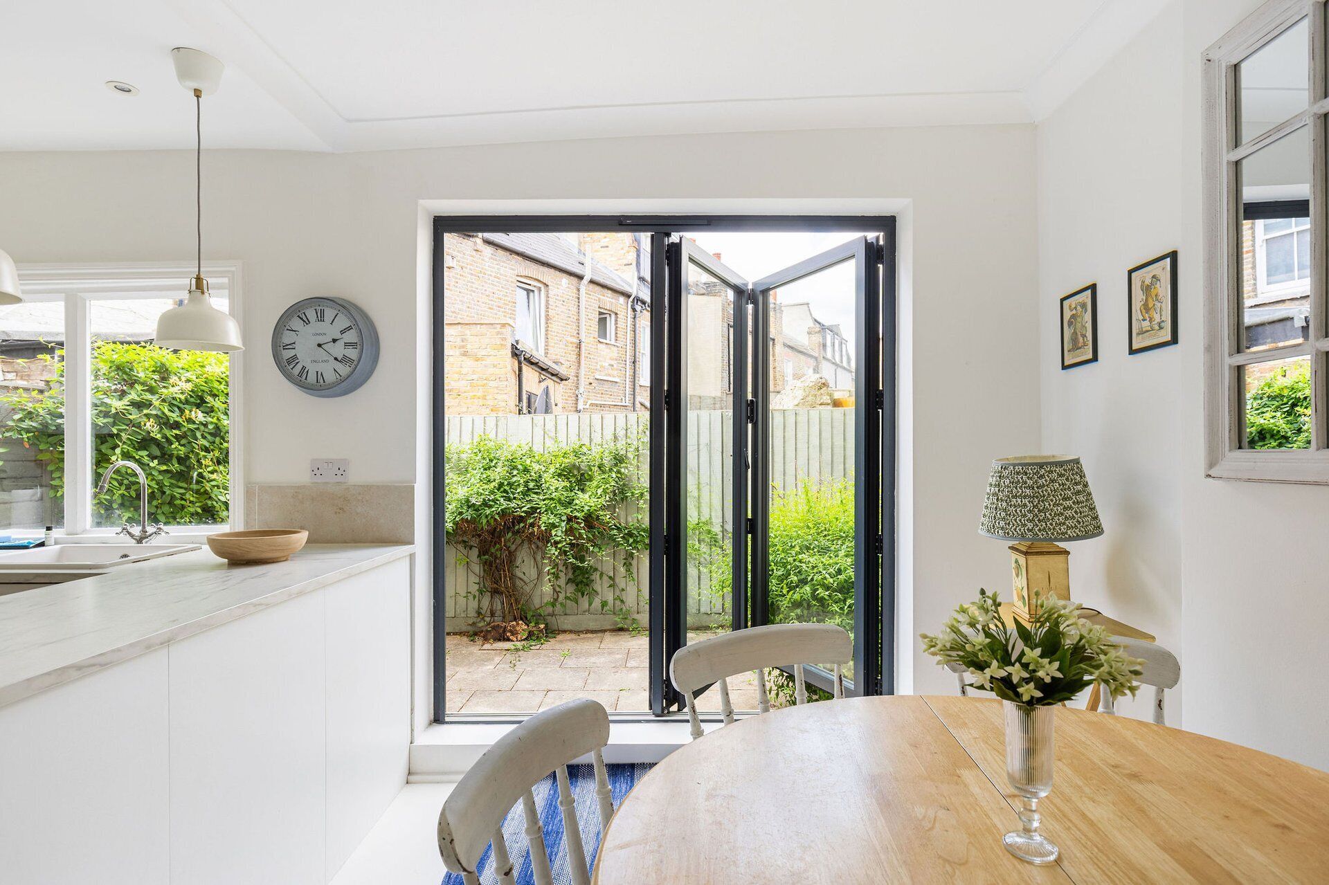A kitchen with a dining area, a clock, and a view of the outside.
