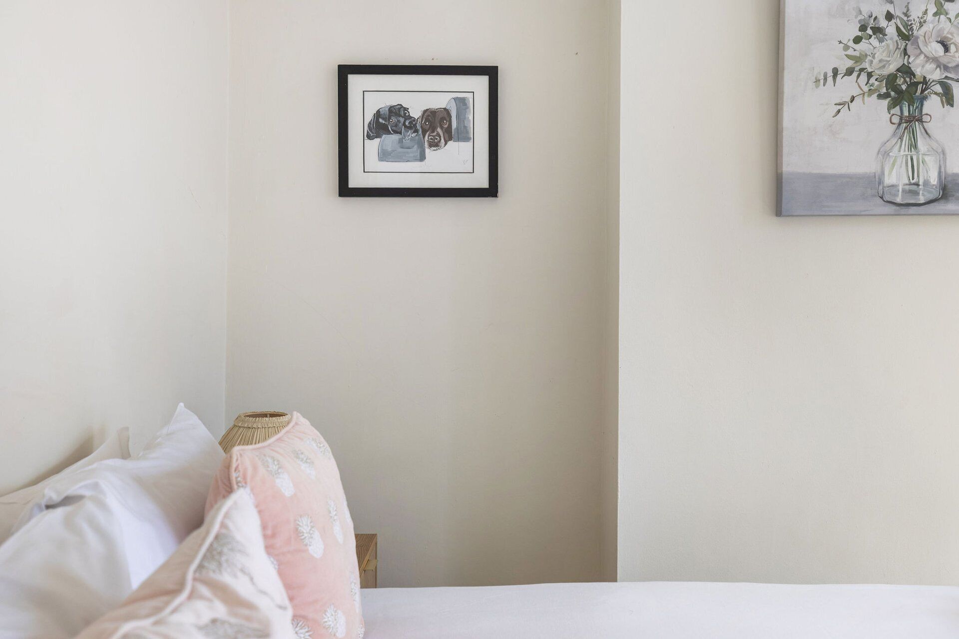 A bedroom with a bed, pillows, a framed picture on the wall, and a vase with flowers.