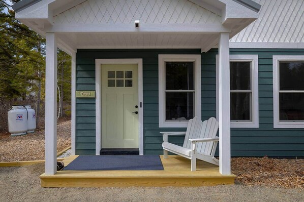 A house with a green exterior, a white porch, a door with a sign, and two white chairs.