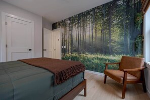 A bedroom with a bed, a chair, and a forest mural on the wall.