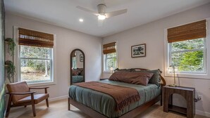 Une chambre à coucher comprenant un lit, une chaise, une table de chevet, un miroir et des fenêtres équipées de stores.