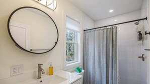 Une salle de bain avec un miroir rond, un lavabo, des toilettes et un espace douche.