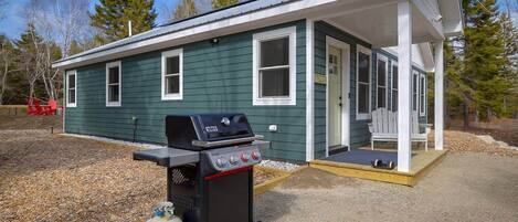 A small, single-story building with a porch and a barbecue grill in front.