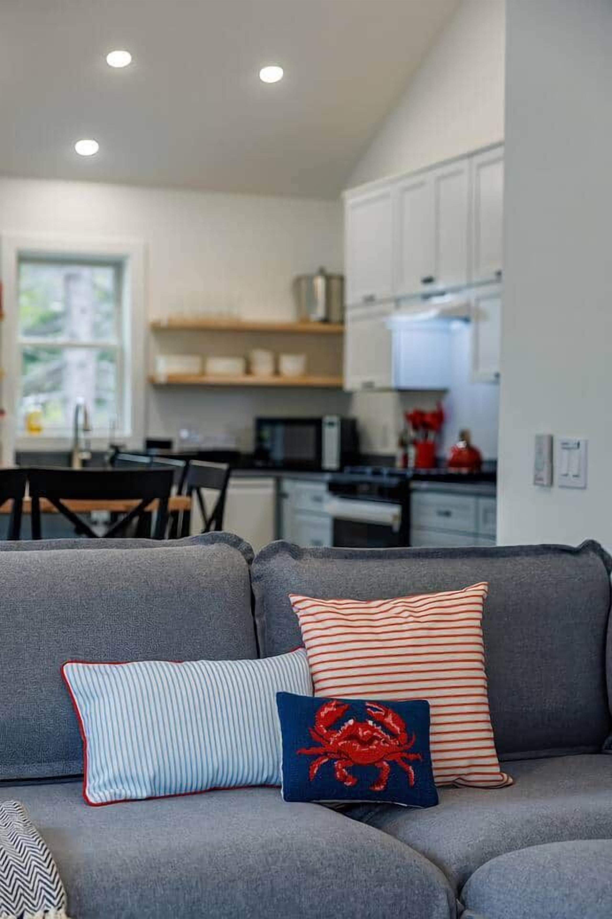 Ein modernes Wohnzimmer mit einem grauen Sofa, gestreiften Kissen und einem roten Design mit Krabbenmotiven.