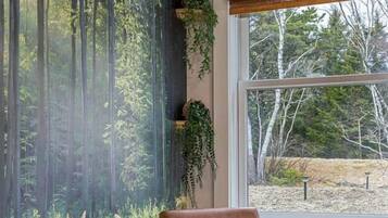 A room with a large window, a chair, and a wall mural of a forest.