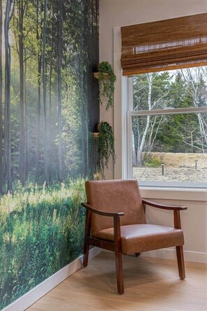 A room with a large window, a chair, and a wall mural of a forest.