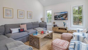 Un salon moderne avec un canapé gris, un pouf à rayures et une table basse en bois.