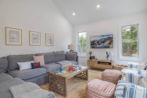 A modern living room with a grey sofa, striped ottoman, and a wooden coffee table. - Ecodia: Eco conscious stay near Acadia NP (Tremont)
