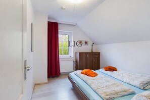 A bedroom with two beds, a window with red curtains, a radiator, and a wooden wardrobe. - Holiday apartment Laughing Gull (Langeoog)