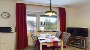 A dining area with a table set for two, a television, and a cabinet with a microwave. - Holiday apartment Laughing Gull (Langeoog)