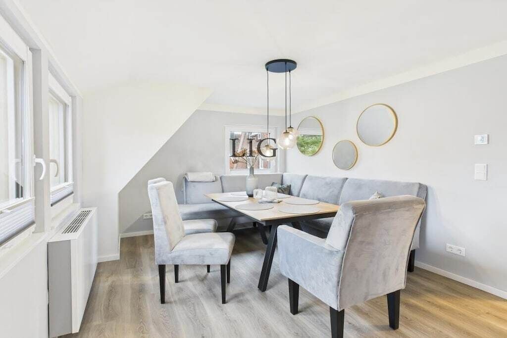 Un coin repas avec une table dressée pour quatre personnes, des chaises de couleur claire et un luminaire suspendu moderne.