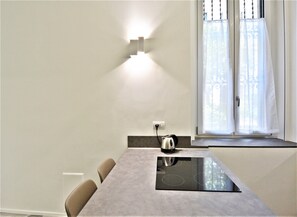 A modern kitchen with a built-in induction cooktop, a kettle, and a window with decorative curtains. - Milano Apartments Lombardini (Milano)