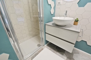 Ein Badezimmer mit einer Duschkabine aus Glas, einem weißen Waschbecken mit Hohlkörperbecken und einer kleinen Topfpflanze auf der Ablagefläche.