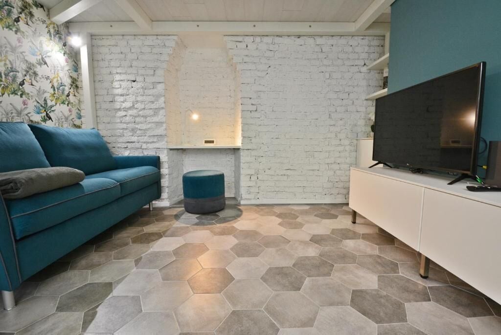 A living room with a sofa, ottoman, TV, and white brick wall.