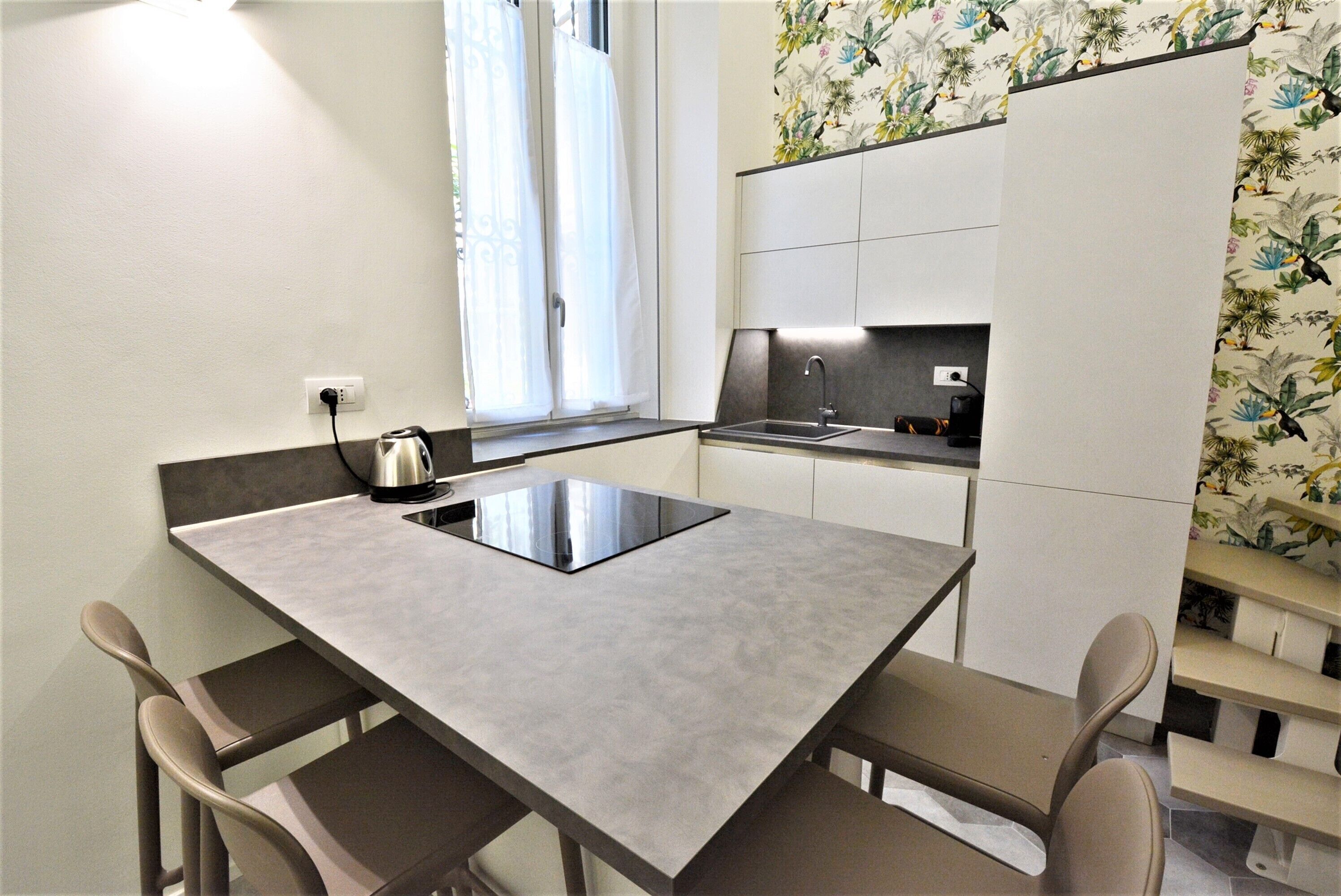 A compact kitchen with a modern design, featuring a built-in stove, a sink, and a window with curtains.