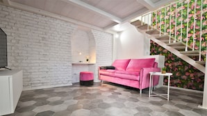 En modern inredning med en vit tegelvägg, en rosa soffa, en trappa med tropisk lövmönstrad tapet och ett hexagonalt klinkergolv.