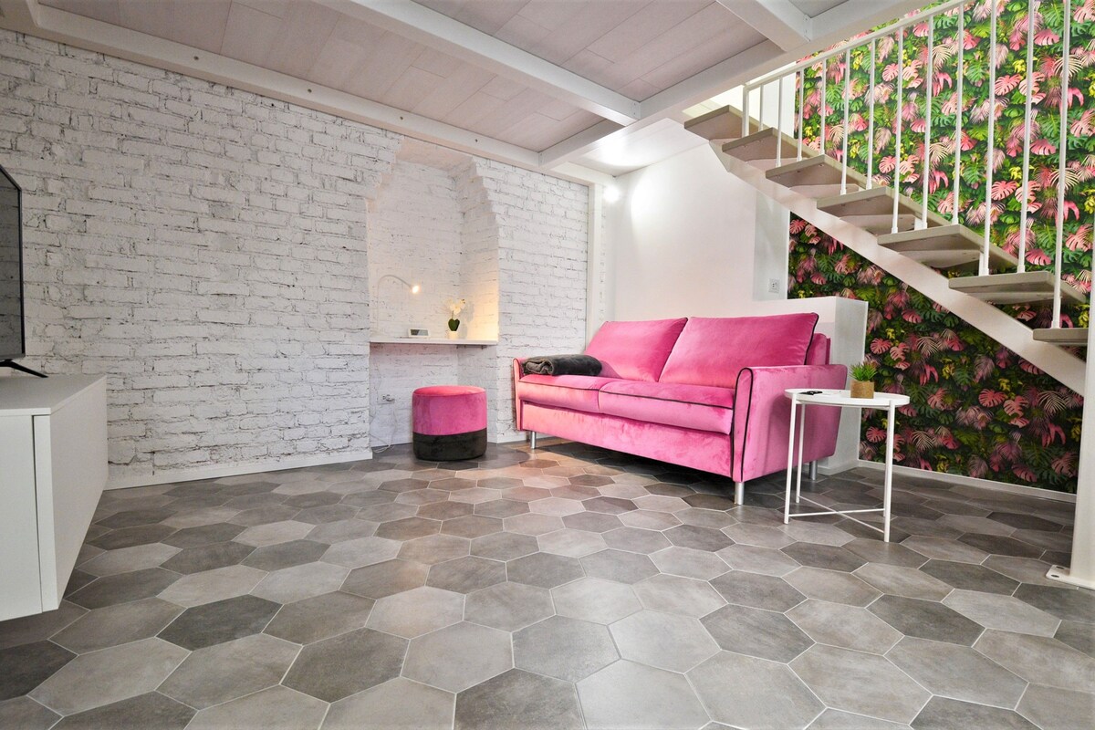 Ein modernes Interieur mit einer weißen Backsteinwand, einem rosafarbenen Sofa, einer Treppe mit tropischem Blattentapete und einem sechseckigen Fliesenboden.
