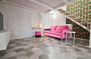 Ein modernes Interieur mit einer weißen Backsteinwand, einem rosafarbenen Sofa, einer Treppe mit tropischem Blattentapete und einem sechseckigen Fliesenboden.