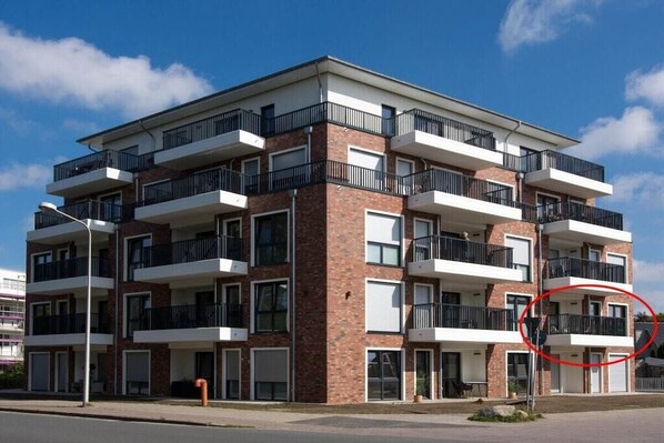 Een meerlaags woongebouw met balkons, een bakstenen gevel en een heldere lucht.