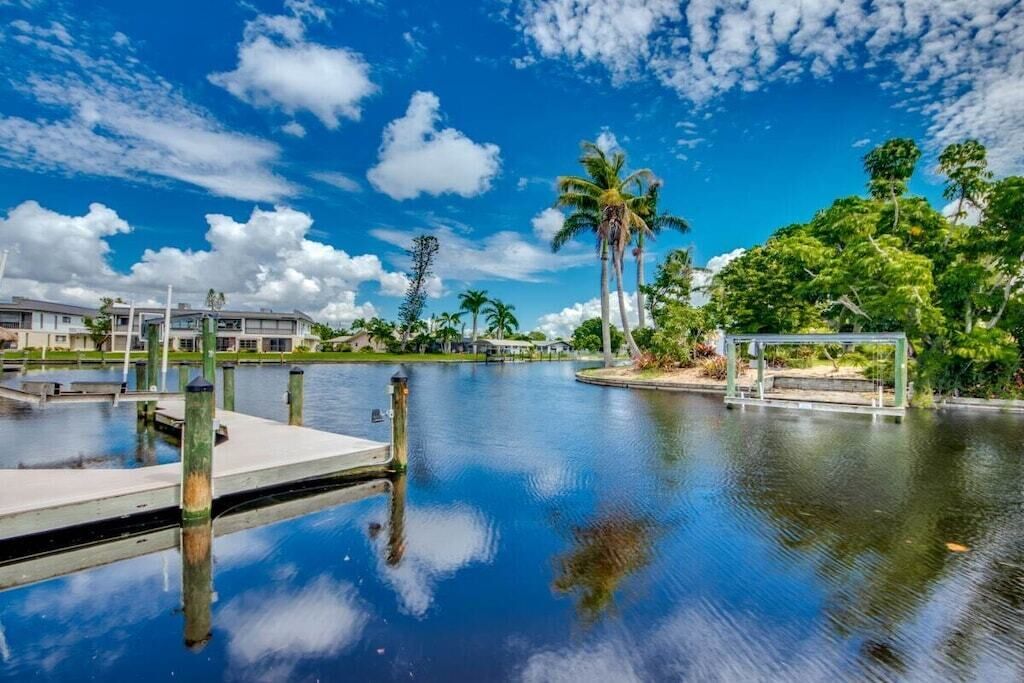A calm water body with a dock, surrounded by greenery and buildings.