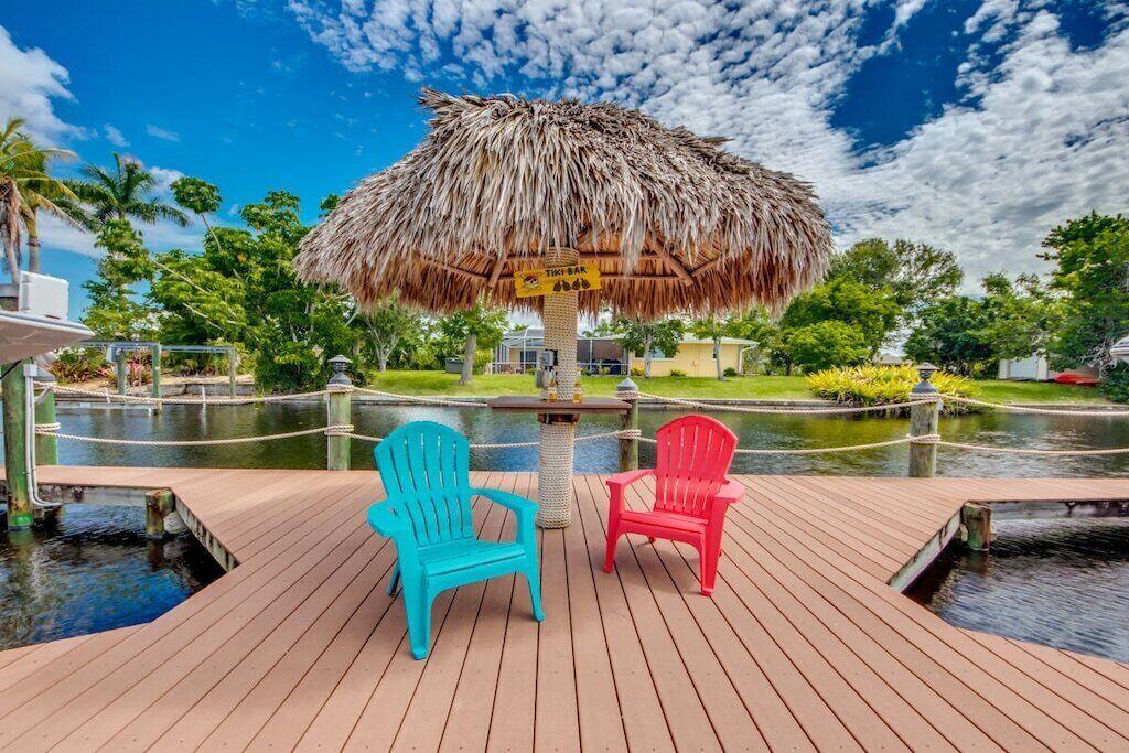 A wooden deck with two chairs, a thatched umbrella, and a water feature.