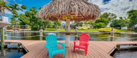 A wooden deck with two chairs, a thatched umbrella, and a water feature.
