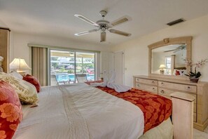 Ein Hotelzimmer mit Bett, Deckenventilator, großem Spiegel, Kommode und Blick auf einen Pool durch eine Schiebetür.