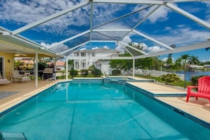 Una piscina blava i cristal·lina amb una zona coberta, envoltada d'una tanca blanca i una cadira vermella.