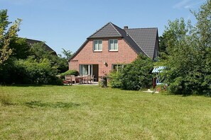 Una casa a due piani in mattoni con tetto spiovente, un portico con sedie e un piccolo giardino.