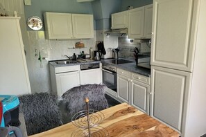 A compact kitchen with white cabinets, a wooden dining table, and a gray furry stool. - Holiday apartment with 3 bedrooms (Langelsheim)