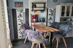 Zona de menjador amb taula i cadires de fusta, una màquina de cafè i una estanteria amb tasses de diferents colors.