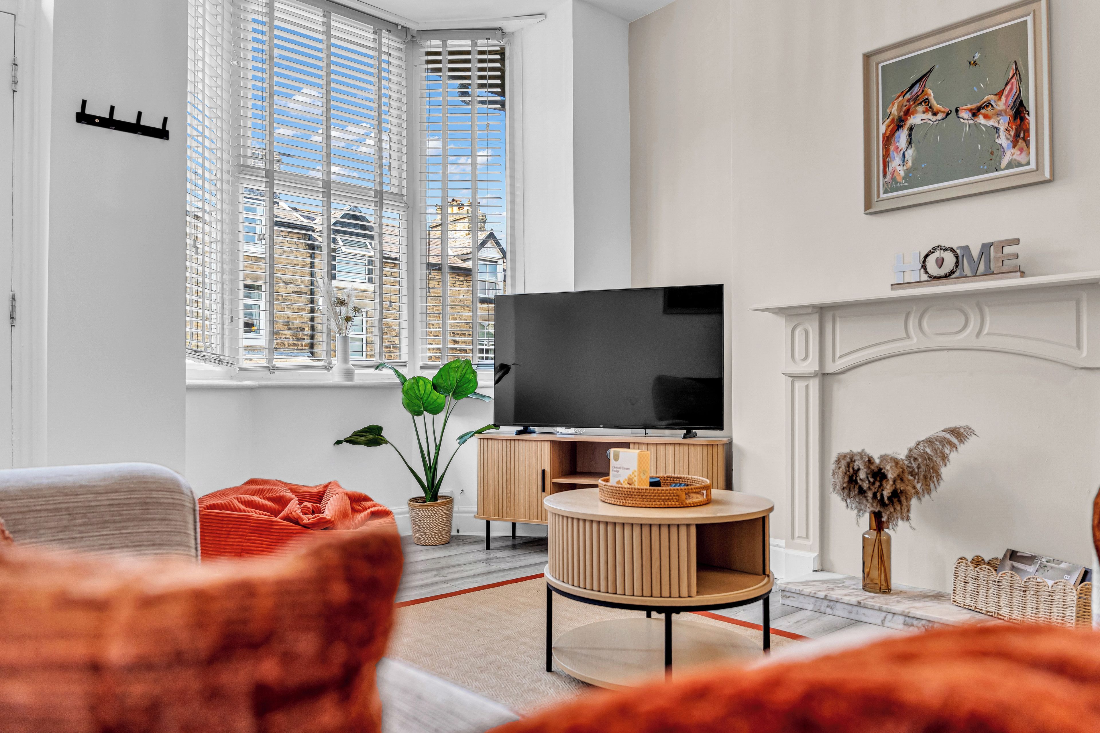 Una sala de estar moderna con televisor, chimenea y un amplio ventanal con persianas.