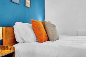 Una cama con ropa blanca, un cabecero de madera y tres almohadas en blanco, naranja y gris.