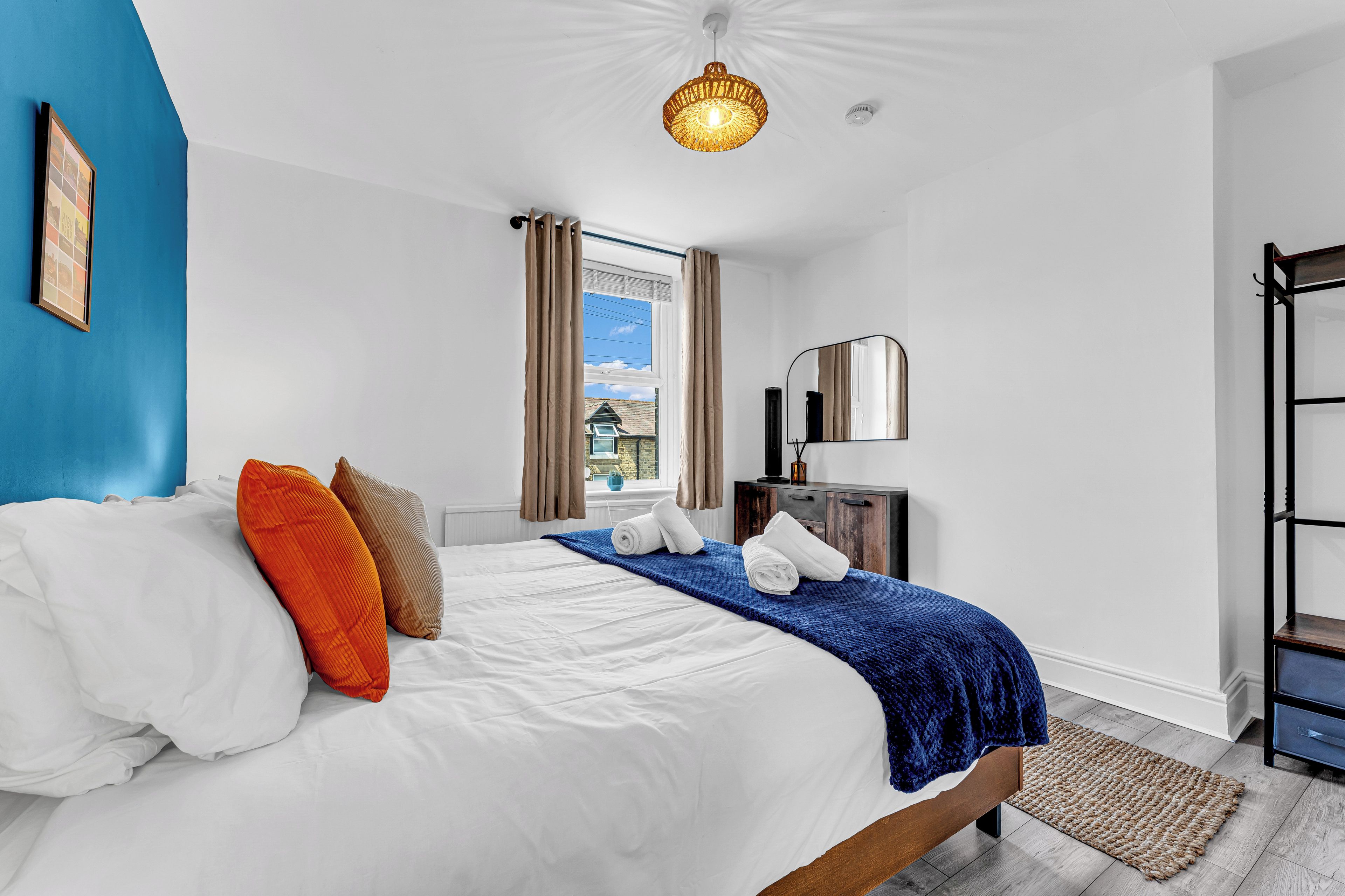Une chambre à coucher avec un lit, une fenêtre avec des rideaux, une table de chevet avec une lampe, et une vue sur l’extérieur.