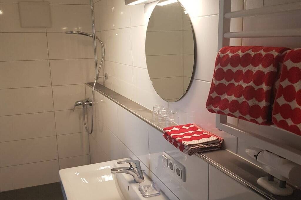 Ett badrum med ett vitt handfat, en spegel, en handdukshängare med en röd handduk och en duschhörna.