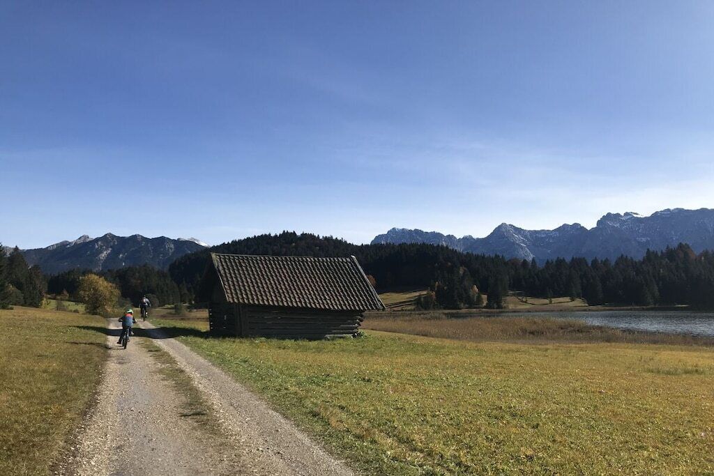 Ländliche Landschaft mit einem Schotterweg, einer Holzhütte und Bergen im Hintergrund.