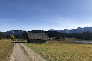 Ländliche Landschaft mit einem Schotterweg, einer Holzhütte und Bergen im Hintergrund.