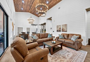 Ein geräumiges Wohnzimmer mit Holzbalkendecke, einer großen braunen Ledersitzgruppe, einem Couchtisch und einem gemusterten Teppich.