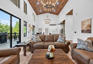 A spacious living area with a large brown leather sofa, a wooden coffee table, and a chandelier. - EV Charger | Hot Tub | Games | Sleeps 16 (Broken Bow)